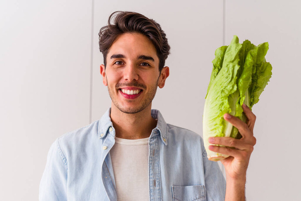 Young mixed race man holding lettuce in his kitchen - Foto, imagen
