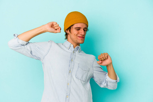 Young caucasian man with make up isolated on blue background  stretching arms, relaxed position. - Photo, Image