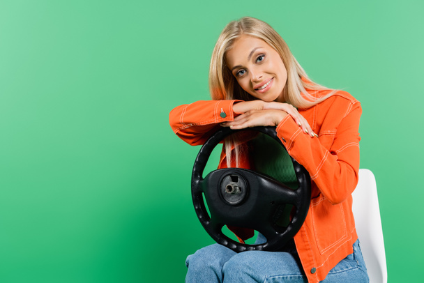 χαρούμενη γυναίκα κάθεται στην καρέκλα και ακουμπά στο τιμόνι απομονωμένη στο πράσινο - Φωτογραφία, εικόνα