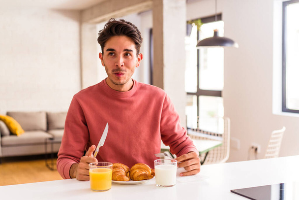 朝にキッチンでクロワッサンを食べる若い混合人種の男 - 写真・画像