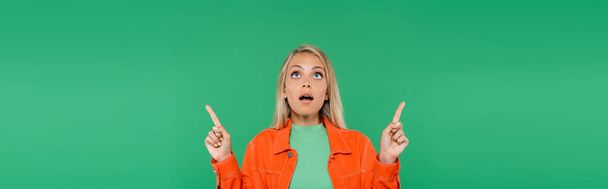 thrilled woman with open mouth pointing with fingers while looking up isolated on green, banner - Foto, Imagen