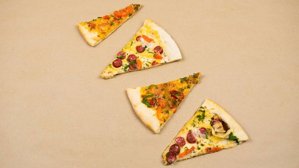 Cuatro rebanadas triangulares de diferentes tipos de pizza sobre un fondo de papel kraft beige. Concepto de una comida deliciosa popular. - Foto, Imagen