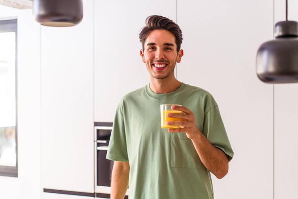 Genç melez adam mutfağında portakal suyu içiyor. - Fotoğraf, Görsel