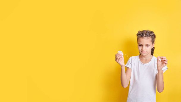 beautiful brown-haired teenager girl holding dental floss on yellow background, children oral hygiene concept copy space banner - Φωτογραφία, εικόνα