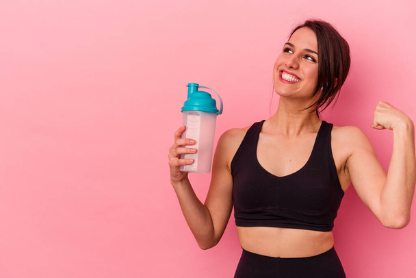 Young caucasian woman drinking a protein shake isolated on pink background raising fist after a victory, winner concept. - Photo, Image