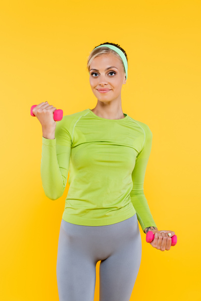 happy woman in green long sleeve t-shirt training with dumbbells isolated on yellow - Photo, Image