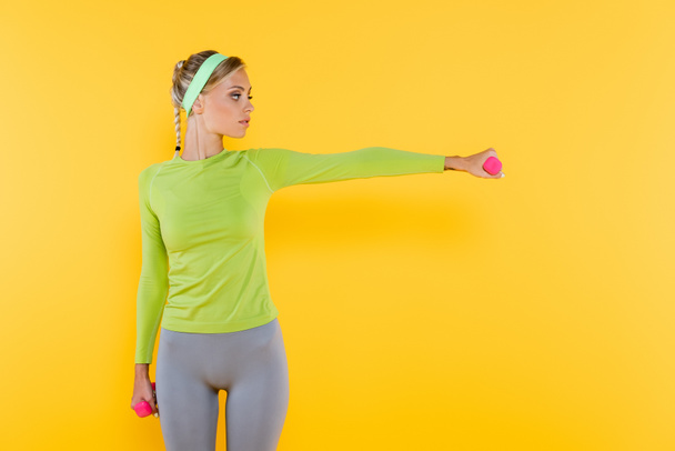 jonge vrouw in groen t-shirt met lange mouwen training met halters geïsoleerd op geel - Foto, afbeelding