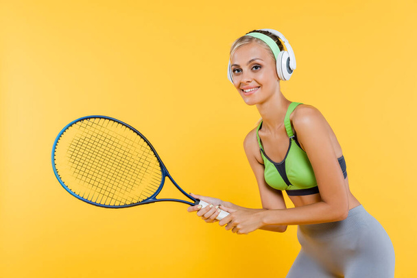 smiling sportswoman in headphones playing tennis isolated on yellow - Fotografie, Obrázek
