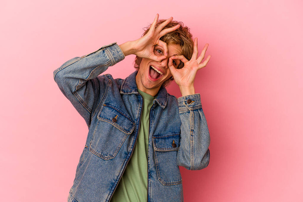 Молодой белый человек с макияжем изолированы на розовом фоне показывая хорошо знак над глазами - Фото, изображение
