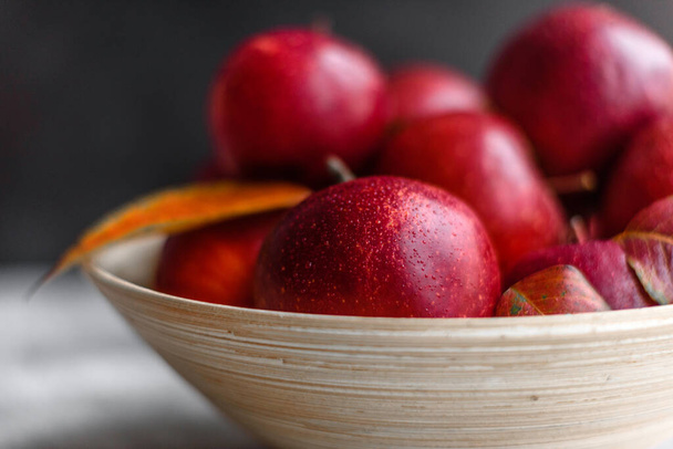 Krásná čerstvá červená jablka s podzimními listy v dřevěné váze na lehkém betonovém stole. Období sklizně - Fotografie, Obrázek