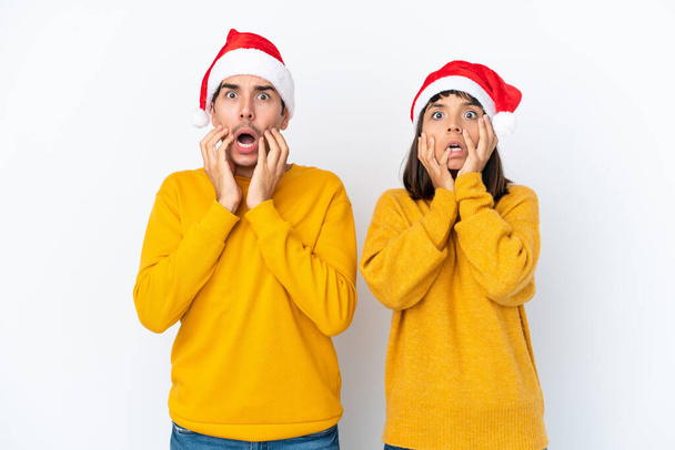 Giovane coppia di razza mista che celebra il Natale isolato su sfondo bianco sorpreso e scioccato mentre guarda a destra - Foto, immagini