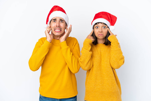 jong gemengd ras paar vieren Kerstmis geïsoleerd op witte achtergrond bedekken beide oren met handen - Foto, afbeelding