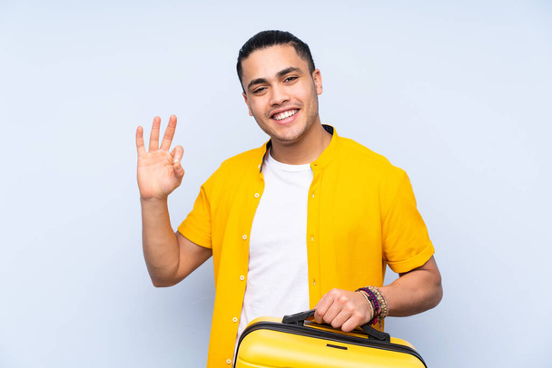 Азиатский красивый мужчина изолирован на синем фоне в отпуске с чемоданом - Фото, изображение