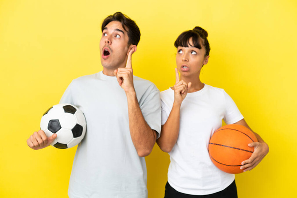 Futbol ve basketbol oynayan genç bir çift sarı arka planda izole edilmiş bir şekilde parmak kaldırmayı düşünüyorlar. - Fotoğraf, Görsel