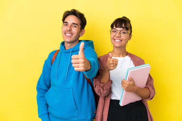 Молода студентська пара ізольована на жовтому тлі, даючи великі пальці вгору жестом, тому що сталося щось хороше
 - Фото, зображення