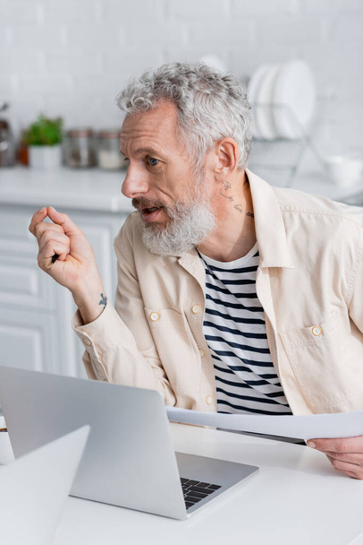 Mature man holding documents near laptops at home  - Foto, imagen