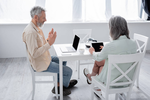 Érett férfi mutatja rendben gesztus alatt videohívás laptop közelében feleség digitális tabletta otthon  - Fotó, kép