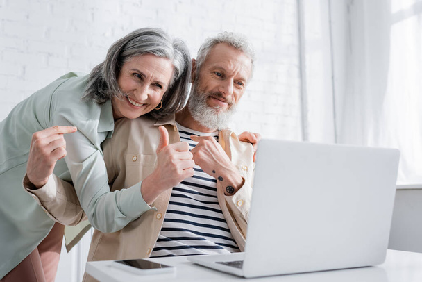 Smiling mature couple gesturing during video call on laptop in kitchen  - Photo, Image