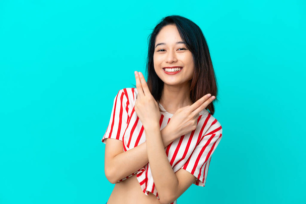 Junge Vietnamesin isoliert auf blauem Hintergrund lächelnd und mit Siegeszeichen - Foto, Bild