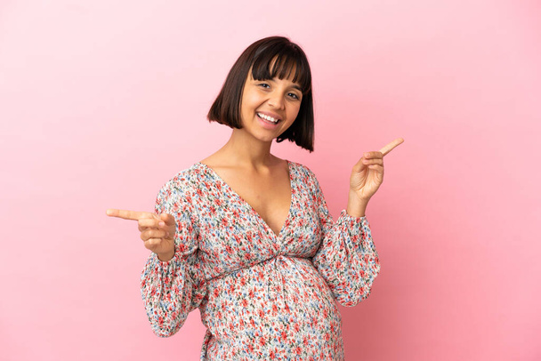 Jovem grávida sobre fundo rosa isolado apontando dedo para as laterais e feliz - Foto, Imagem