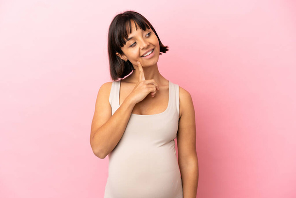 Νεαρή έγκυος γυναίκα πάνω από απομονωμένο ροζ φόντο σκέφτεται μια ιδέα, ενώ ψάχνει επάνω - Φωτογραφία, εικόνα