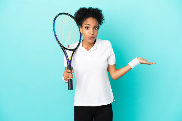 Genç tenisçi kadın mavi arka planda izole edilmiş ve ellerini kaldırırken şüpheleri var. - Fotoğraf, Görsel