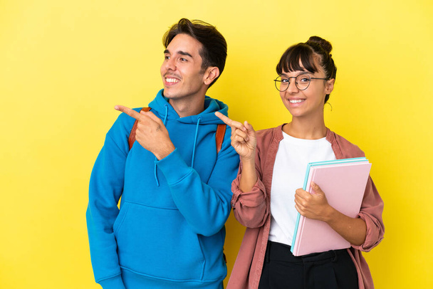 Fiatal diák pár elszigetelt sárga háttér mutató ujját oldalra oldalsó helyzetben - Fotó, kép
