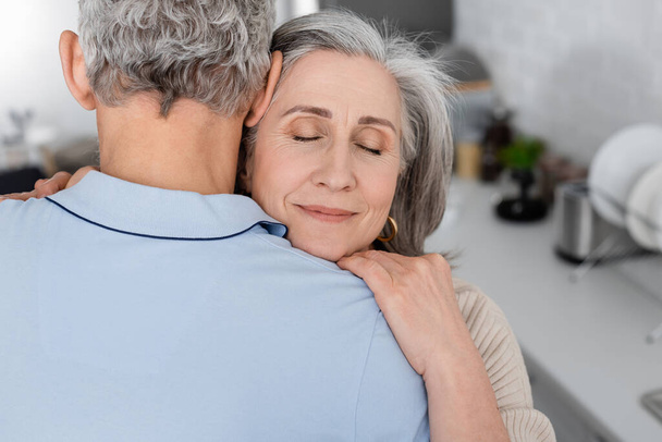 Middle aged woman embracing husband in kitchen  - Photo, Image