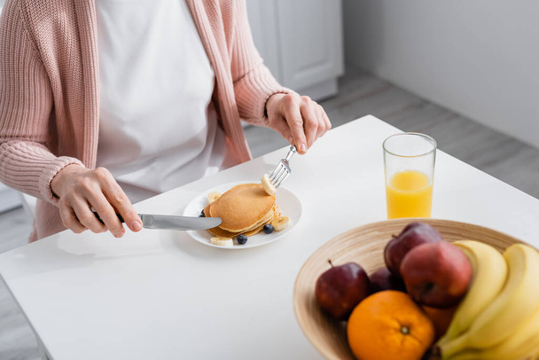 Cropped view of mature woman holding cutlery near pancakes and fruits at home  - Foto, imagen