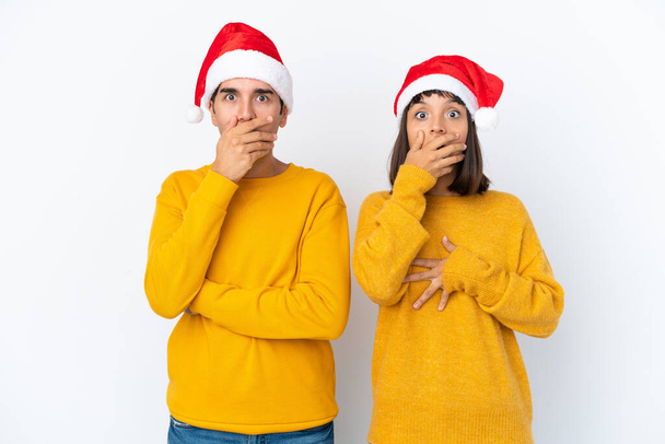 Jeune couple mixte célébrant Noël isolé sur fond blanc couvrant la bouche avec les mains pour avoir dit quelque chose d'inapproprié - Photo, image