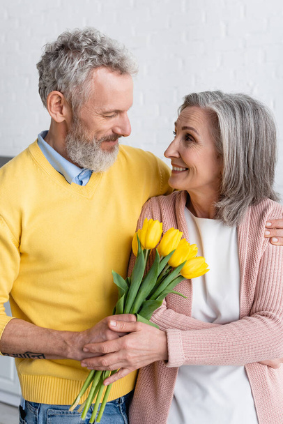 Lächelnde Frau mit Blumen neben bärtigem Ehemann zu Hause  - Foto, Bild