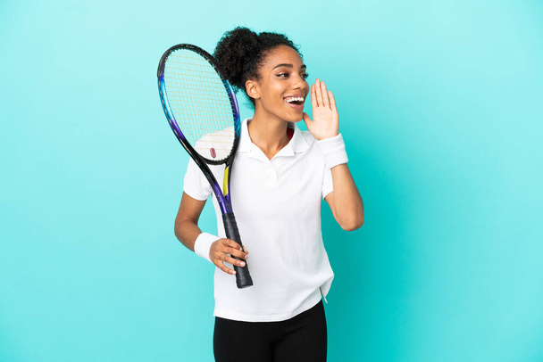 Junge Tennisspielerin isoliert auf blauem Hintergrund schreit mit weit geöffnetem Mund zur Seite - Foto, Bild