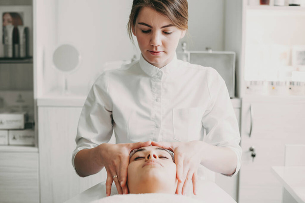 Kosmetička masíruje klientovi čelo, dělá relaxační masáž hlavy v lázeňském salonu. Koncept péče o pleť - Fotografie, Obrázek