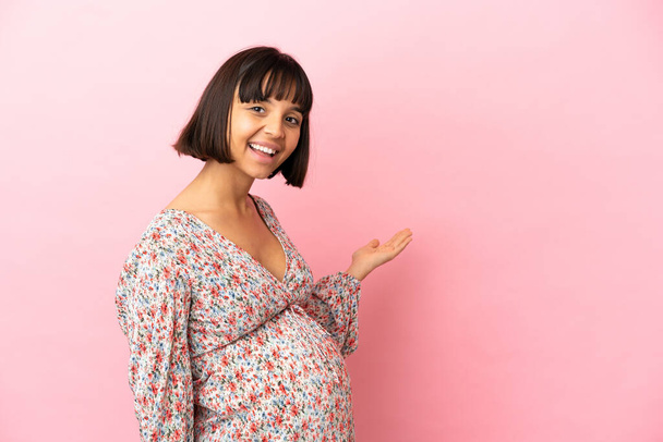 Young pregnant woman over isolated pink background extending hands to the side for inviting to come - Valokuva, kuva