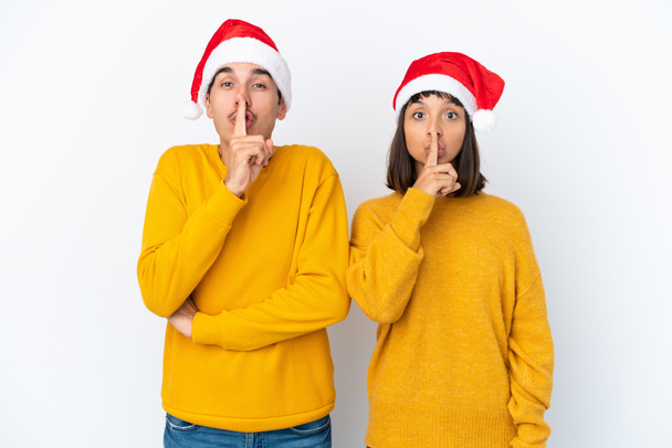 Jeune couple métis célébrant Noël isolé sur fond blanc montrant un signe de silence geste mettre le doigt dans la bouche - Photo, image