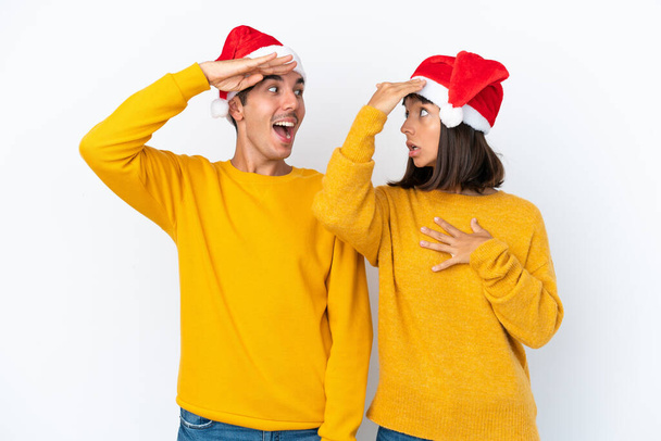 Junges gemischtes Paar feiert Weihnachten isoliert auf weißem Hintergrund mit Überraschung und schockiertem Gesichtsausdruck - Foto, Bild