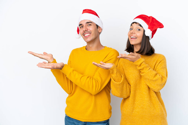 Giovane coppia di razza mista che celebra il Natale isolato su sfondo bianco allungando le mani a lato per invitare a venire - Foto, immagini