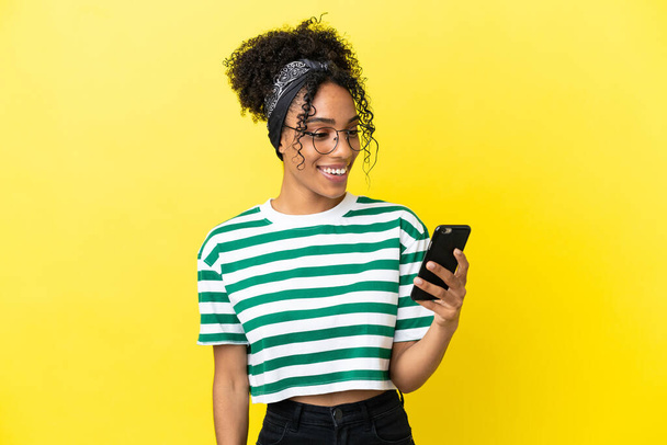Jonge Afrikaanse Amerikaanse vrouw geïsoleerd op gele achtergrond verzenden van een bericht of e-mail met de mobiele - Foto, afbeelding