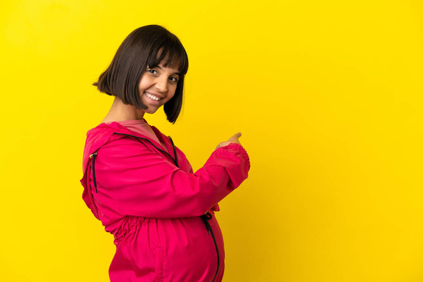 Молода вагітна жінка над ізольованим жовтим тлом, що вказує назад
 - Фото, зображення
