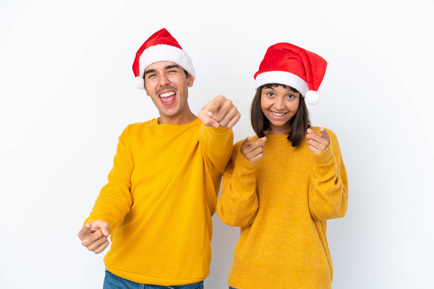 joven mixta raza pareja celebrando Navidad aislado en blanco fondo puntos dedo en usted mientras sonriendo - Foto, imagen