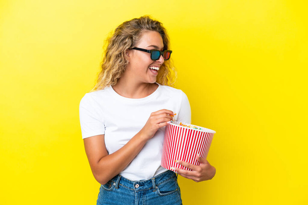 Girl with curly hair isolated on yellow background with 3d glasses and holding a big bucket of popcorns - Photo, Image