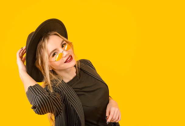  1 young white woman in a black jacket and hat on a yellow background - Foto, afbeelding