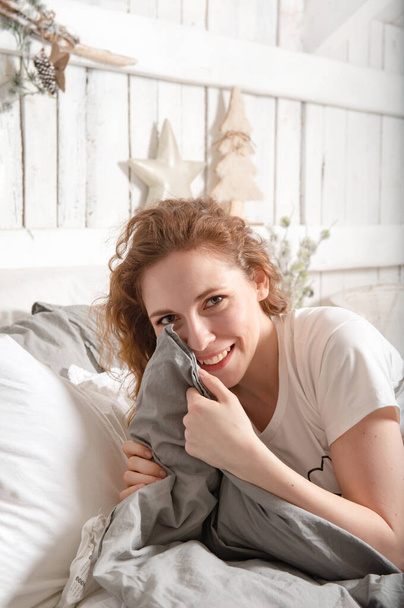 young beautiful woman with red hair in bed smiling, bright room with christmas interior, - Photo, image