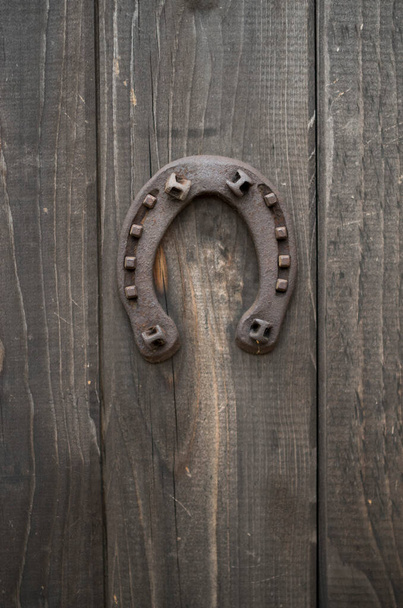 Παλιό σκουριασμένο πέταλο καρφωμένο σε μια μπροστινή ξύλινη πόρτα. - Φωτογραφία, εικόνα