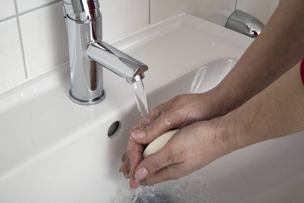 A person washing their hands with soap in a white sink - Photo, Image