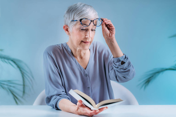 Senior woman with eyeglasses having problems with book reading. Indication for cataracts, glaucoma, and vision loss in the elderly. - 写真・画像