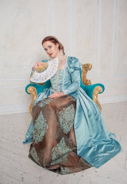 Красива молода жінка в середньовічному стилі блакитна сукня з вентилятором, сидячи в аркаді
 - Фото, зображення