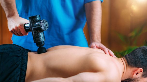 Tratamiento lumbar con pistola de masaje. fisioterapeuta masaje mans inferior espalda   - Foto, imagen