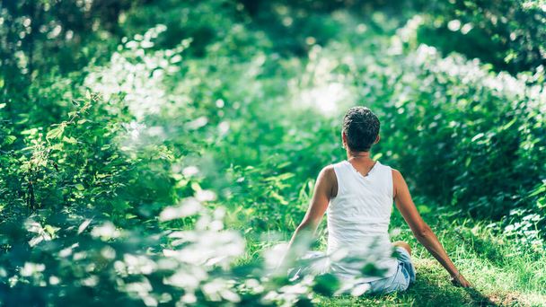 Geest kalmerende innerlijke rust buiten meditatie. Een onherkenbare denkende vrouw mediterend omringd door weelderige, groene vegetatie, die haar kalmte en innerlijke rust vergroot  - Foto, afbeelding