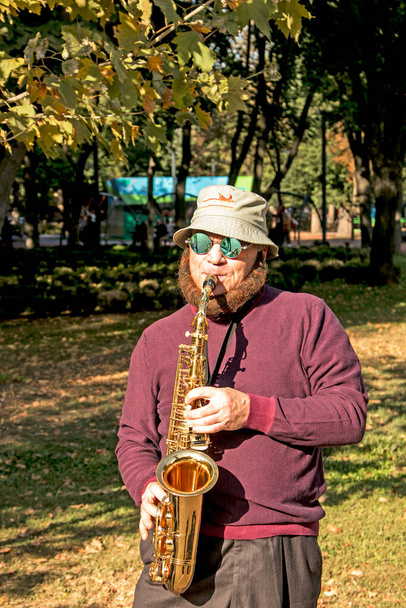 Dnepropetrovsk,ウクライナ- 09.17.2021:男は公園でサックスを再生します.慈善事業のために音楽を演奏サックスとストリートミュージシャン。管楽器による公演 - 写真・画像